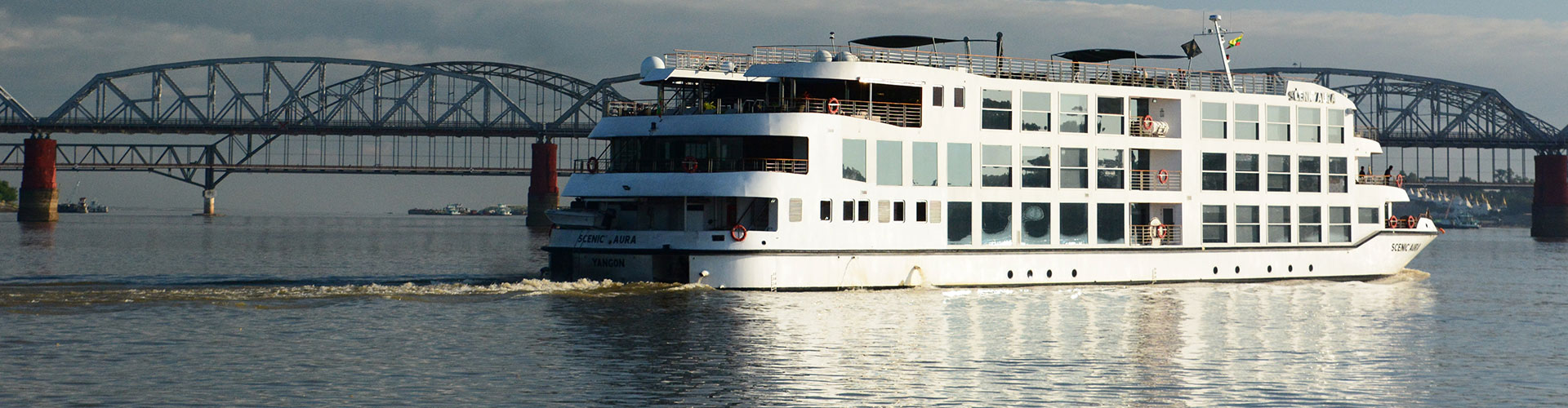 Modern river cruise ship passing a steel truss bridge