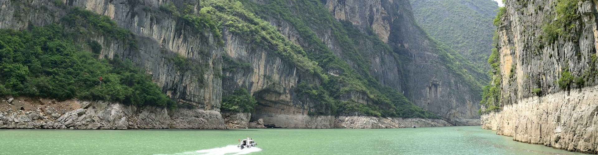 Small boat on a green river beneath towering limestone gorge walls