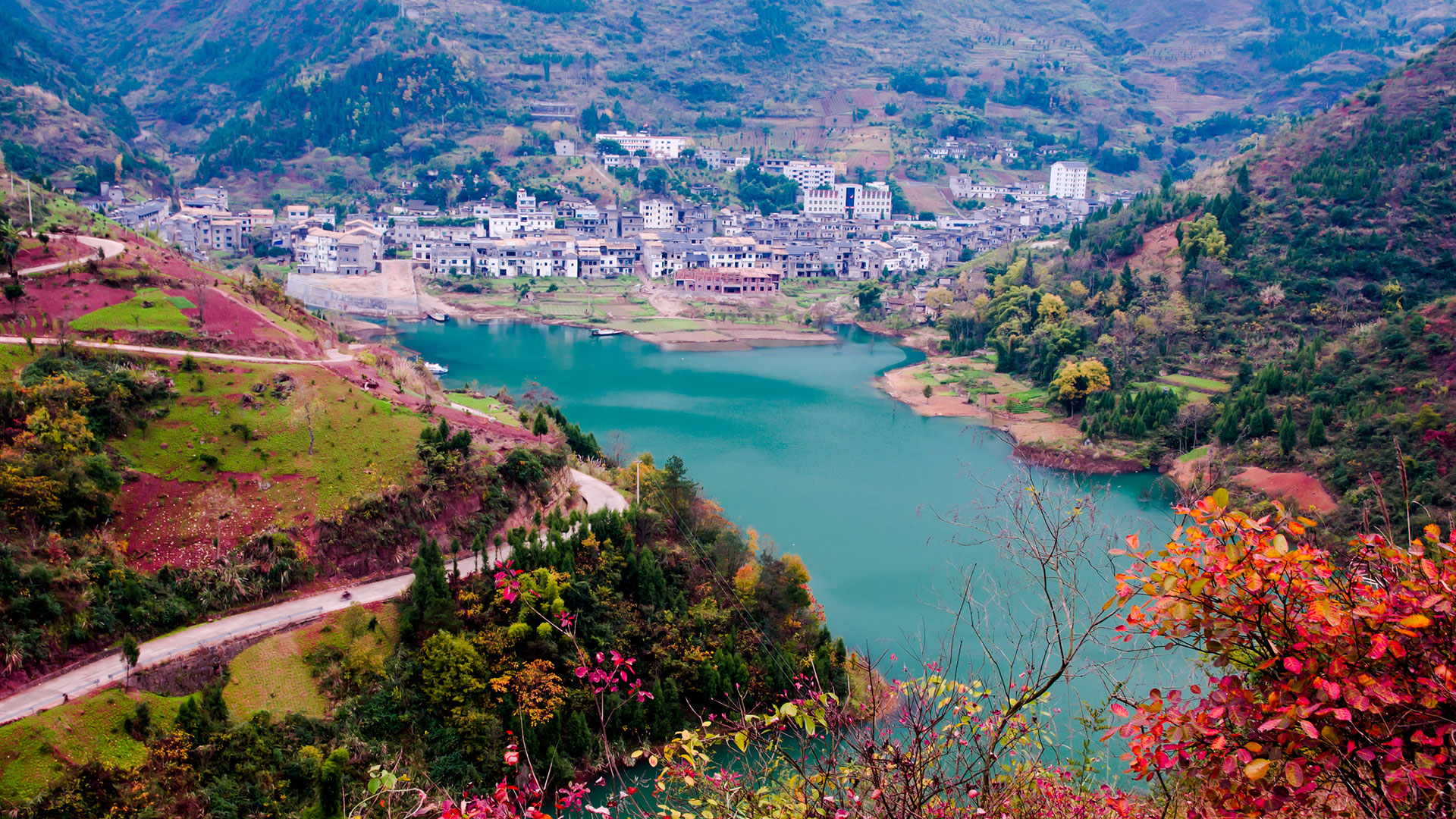 Turquoise river valley with a hillside town and red autumn trees