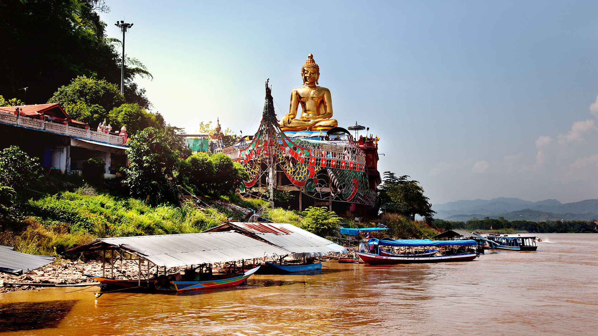 Giant golden Buddha statue above longtail boats on the muddy Mekong