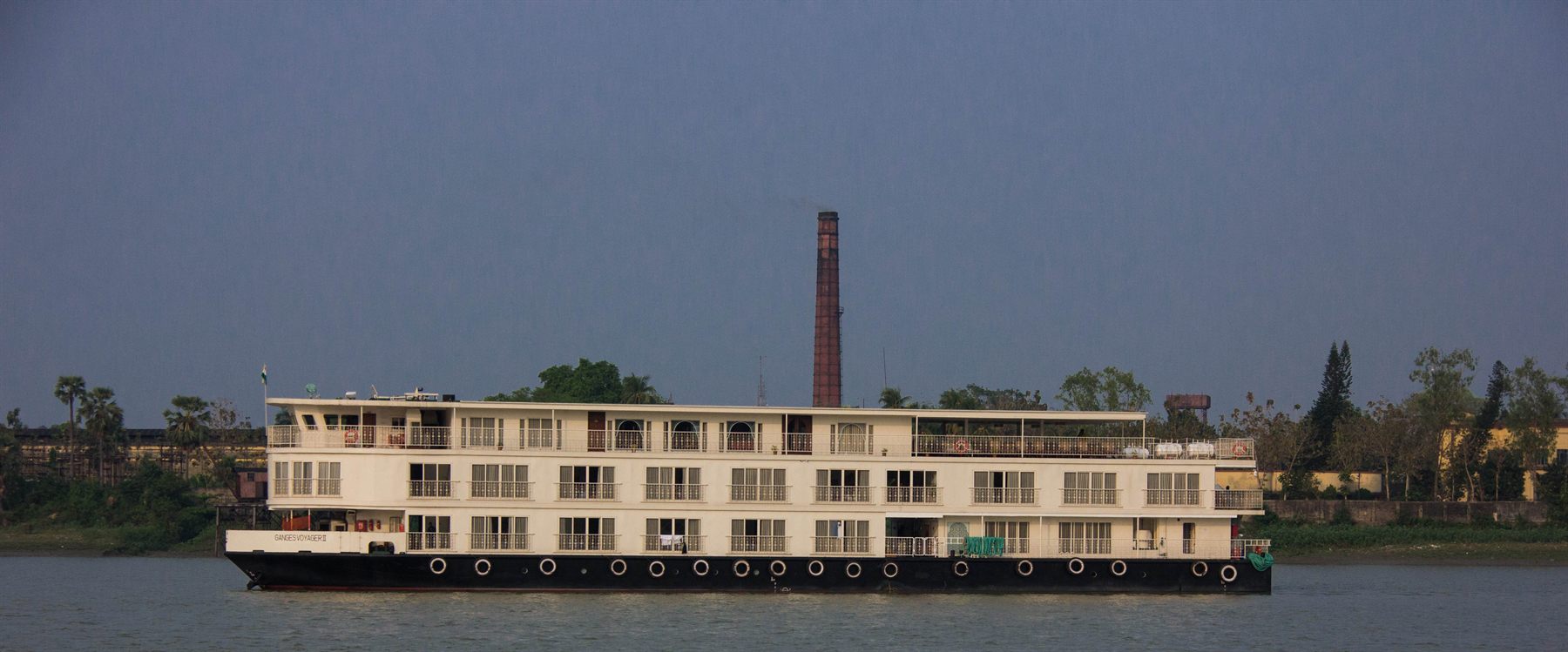 Colonial-style river cruise ship on an Indian river under a stormy sky