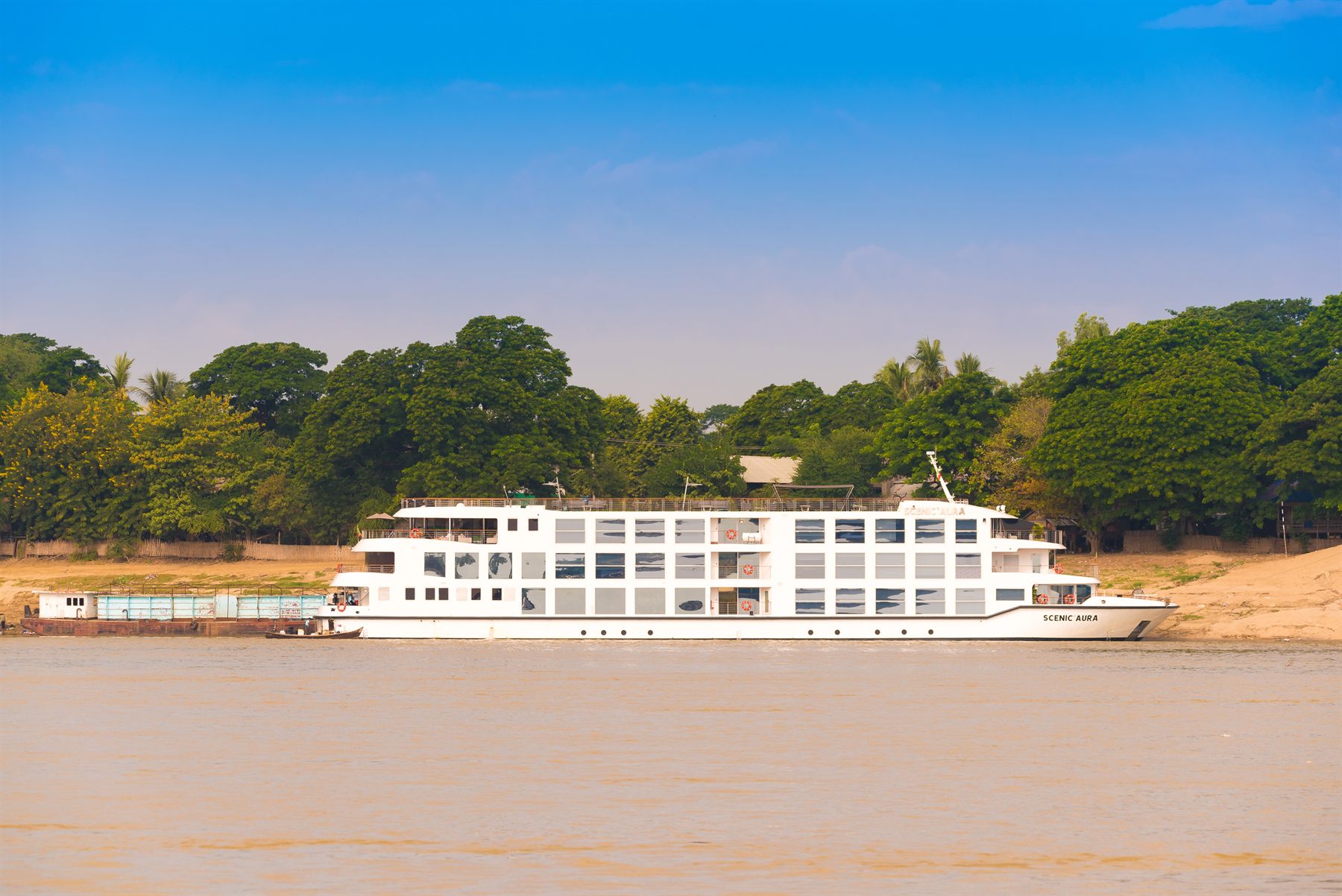 White river cruise ship moored off a sandy, tree-lined riverbank